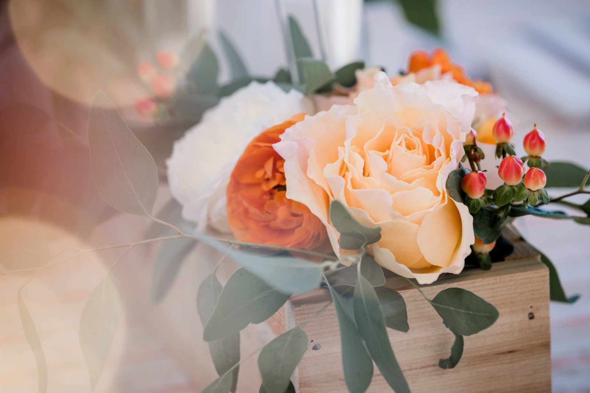 Peach garden roses, white hydrangea, eucalyptus and hypericum berries arranged in a wooden crate